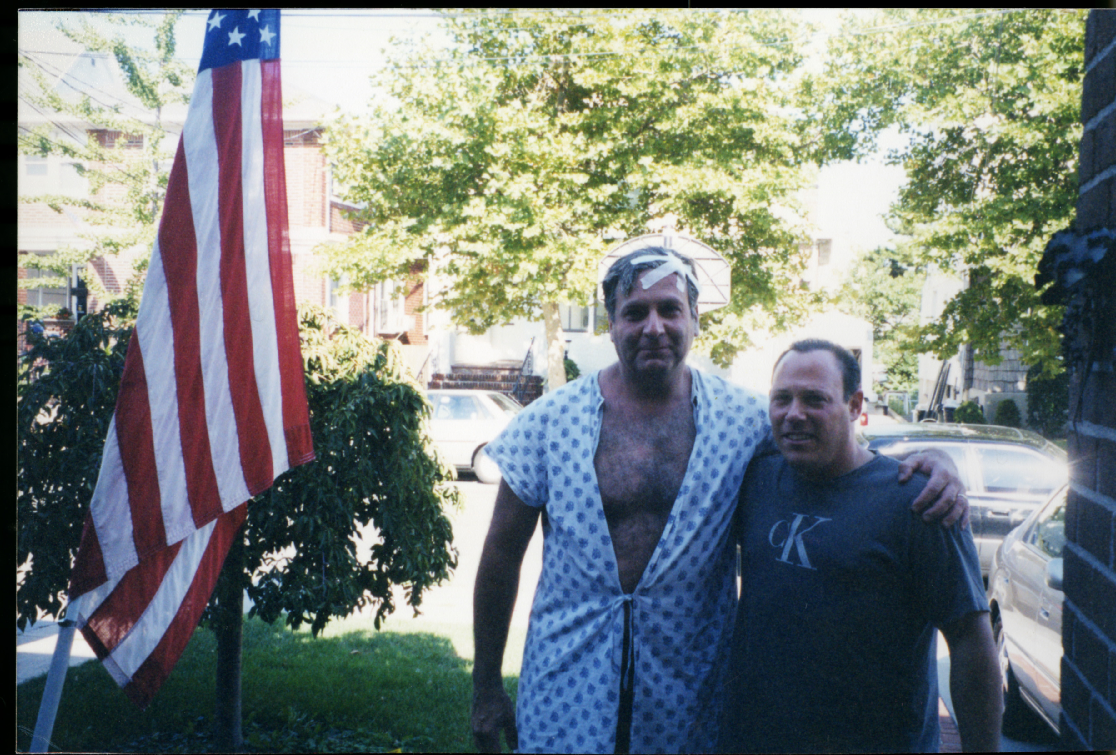Survivor Richard Eichen embraces the stranger who drove him home on September 11, 2001, in the front yard of a home on a sunny day. An American flag stands to the right of them.