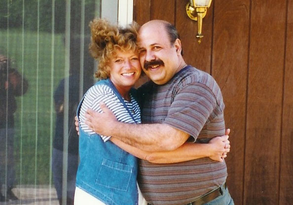 Richard Pecorella and Karen Juday embrace while standing on a porch outside.