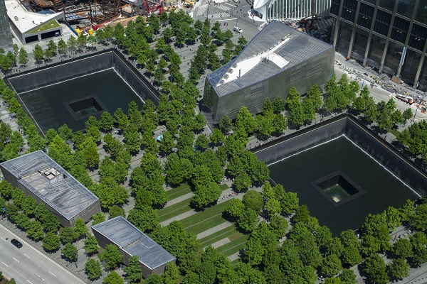 An aerial view of the 9/11 Memorial shows the twin reflecting pools, the Museum pavilion, and the plaza’s many trees and pathways.