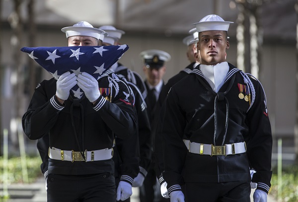 Members of the U.S. Navy stand in formation during a flag-folding ceremony on 9/11 Memorial plaza. One of them is holding up a U.S. flag in front of him.