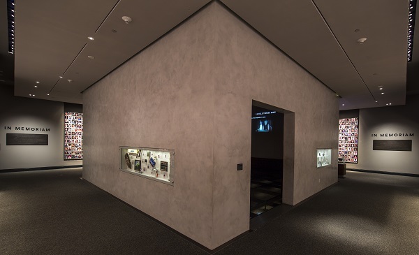 An interior look at the In Memoriam exhibition. Personal artifacts that belonged to victims are displayed on the walls of an inner chamber in which their profiles are projected. Some of the 2,983 portrait photographs of victims are on walls to the left and right of the chamber.