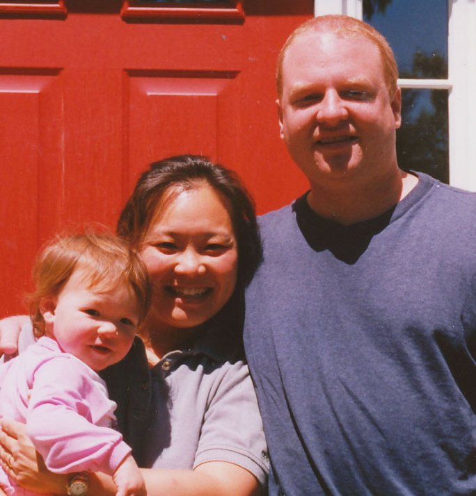 Peter Burton Hanson and his wife Sue Kim Hanson pose for a photo with their toddler-age daughter outside their home in Massachusetts.