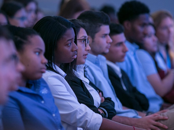 A row of students are seated in the auditorium as they attend an event. 