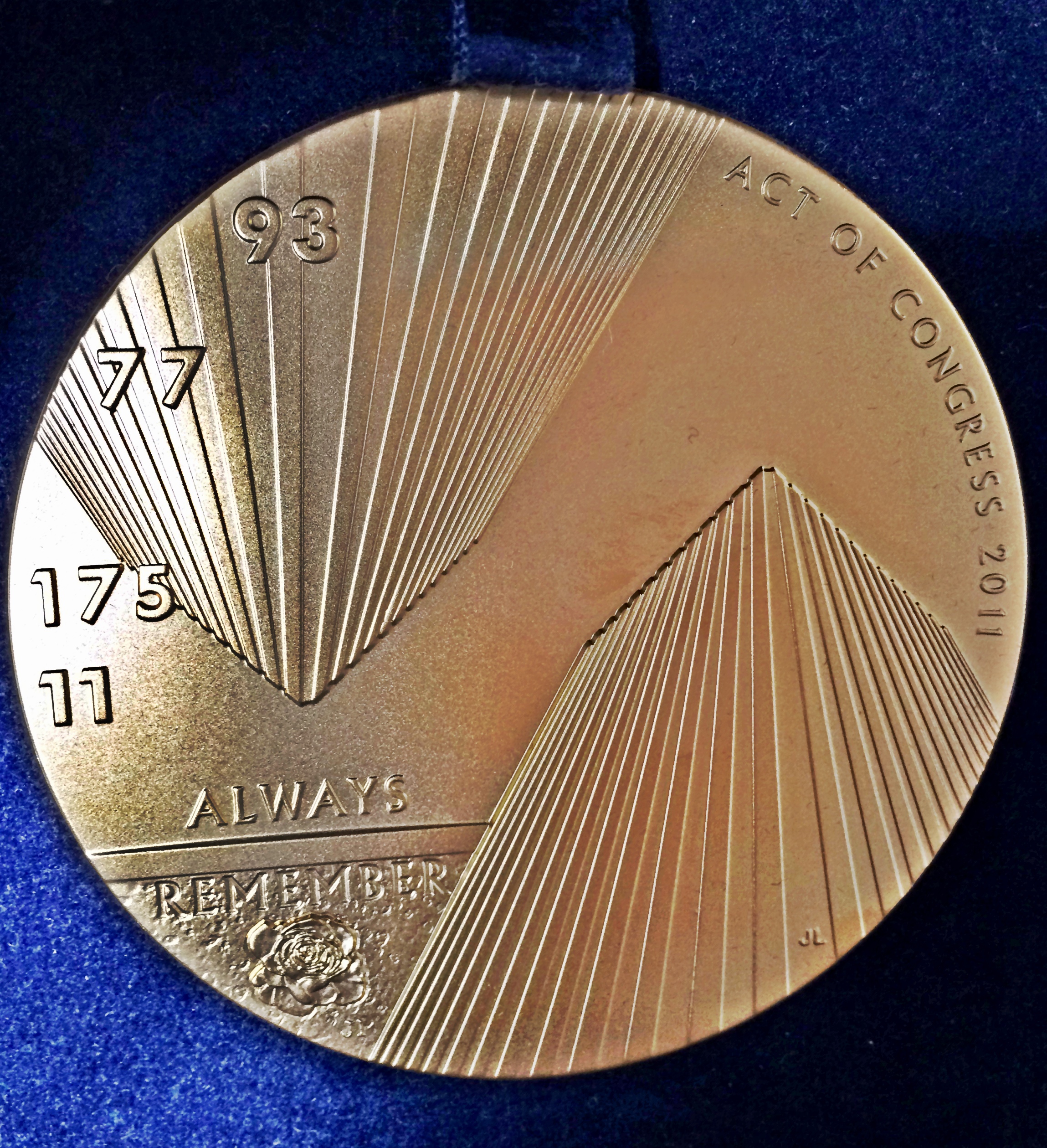 A Congressional Gold Medal given to the 9/11 Memorial Museum is displayed on a blue surface at the Museum. The circular medal is gold and features an engraving of the Twin Towers and the numbers of the four flights that were hijacked. It reads “always remember” and “act of Congress 2011.”