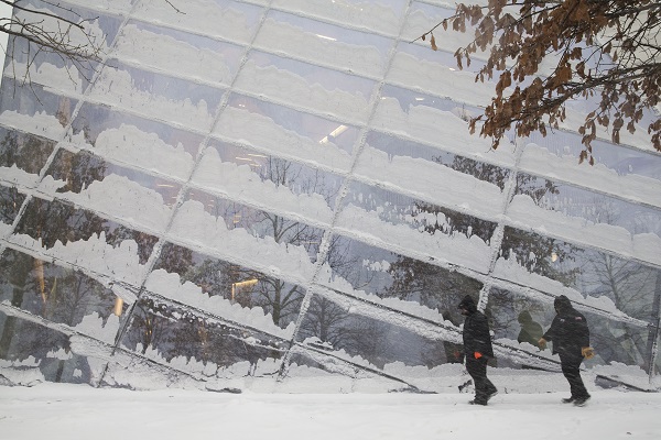 Snow covers the windows of the Museum pavilion as two warmly dressed workers walk by during a winter storm. 