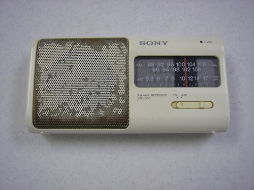 An off-white Sony radio that belonged to James Kazalis is displayed on a white surface at the Museum.