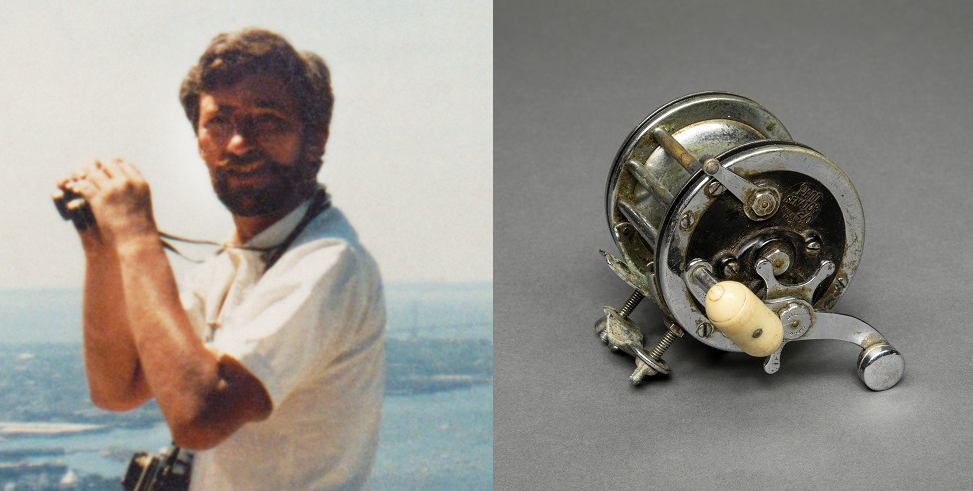 In an old photograph, Stephen A. Knapp looks up from a pair of binoculars and smiles. His fishing reel is also seen displayed on a gray surface.