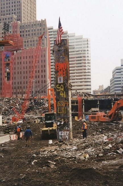 In this historical photo, the Last Column stands at Ground Zero during the cleanup of the site. An American flag has been placed atop the column. Piles of debris and other construction equipment are seen in the background.
