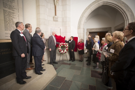 Cornell University’s interim president Hunter Rawlings dedicates a memorial at the university. More than a dozen people are standing in a hallway as Rawlings unveils a wreath.