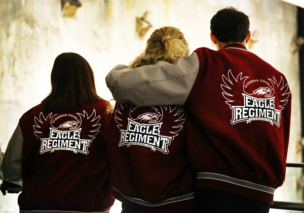 Three high school students from Marjory Stoneman Douglas High School visit the Museum. One of the students has his arm around another as they face away from the camera. The backs of their red letterman jackets read “Eagle Regiment.”