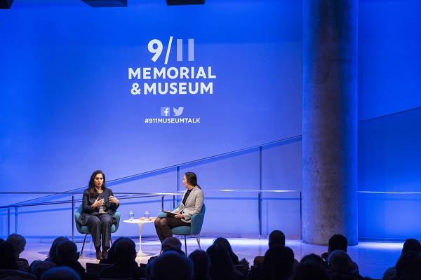 Washington Post correspondent Souad Mekhennet and Jessica Chen, director of public programs at the 9/11 Memorial Museum, speak onstage at the Museum auditorium as an audience watches in the foreground. The stage has been lit a deep blue.