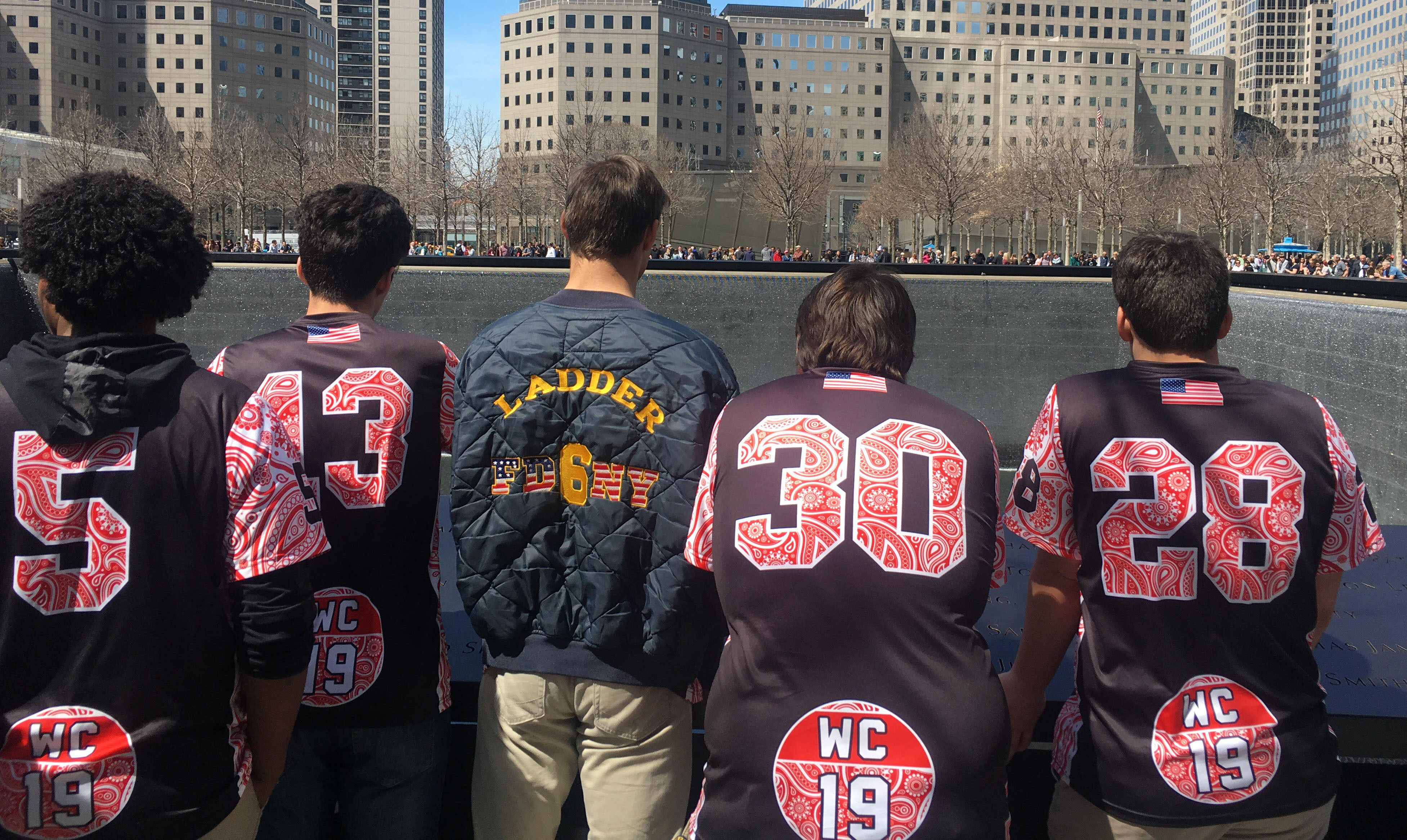 Five members of the Nyack Boys varsity lacrosse team stand beside a reflecting pool at Memorial plaza. They are facing away from the camera as they look down into the pool.