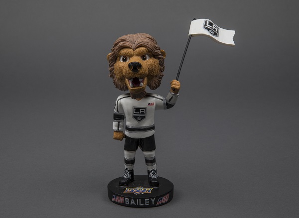 A bobblehead figurine of Los Angeles Kings mascot Bailey is displayed on a gray surface. The mascot is an anthropomorphized lion.