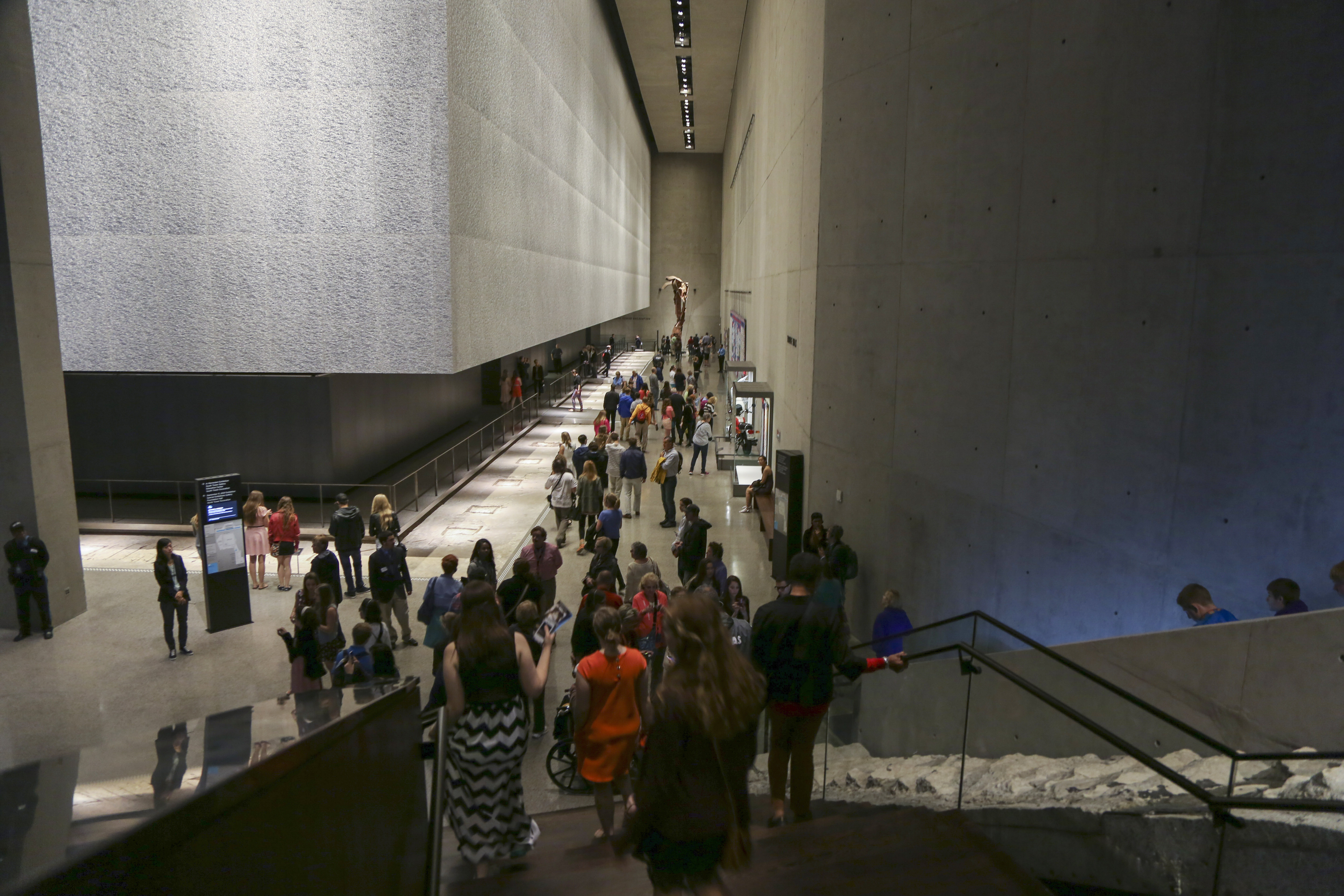 Dozens of visitors are seen in the 9/11 Memorial Museum. In the foreground, visitors pass by the Survivors’ Staircase.