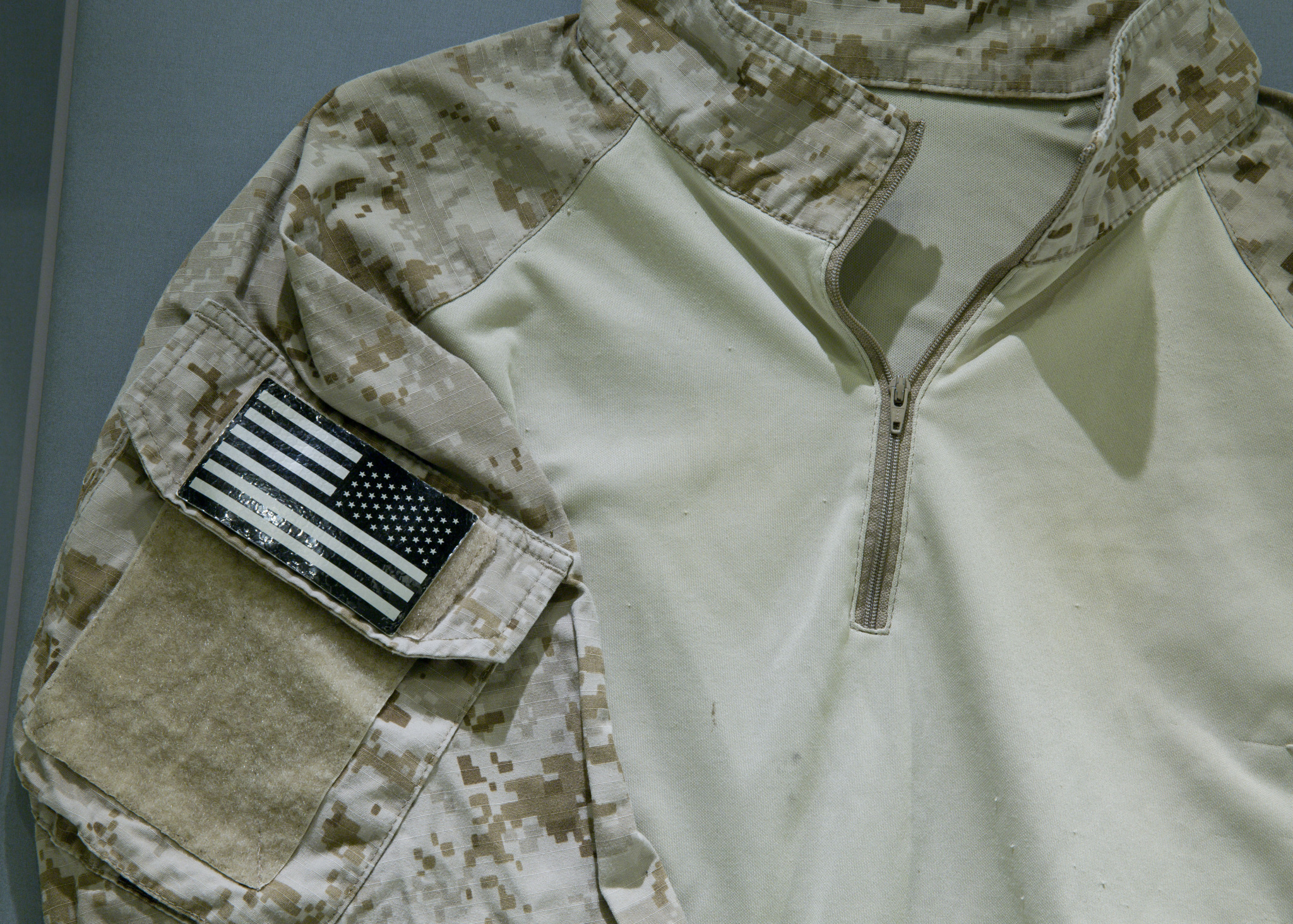 A camouflage uniform shit from a Navy Seal Team 6 member involved in the raid on Osama bin Laden’s compound is displayed at the Museum. A closeup of the tan and brown shirt shows a black and white American flag.