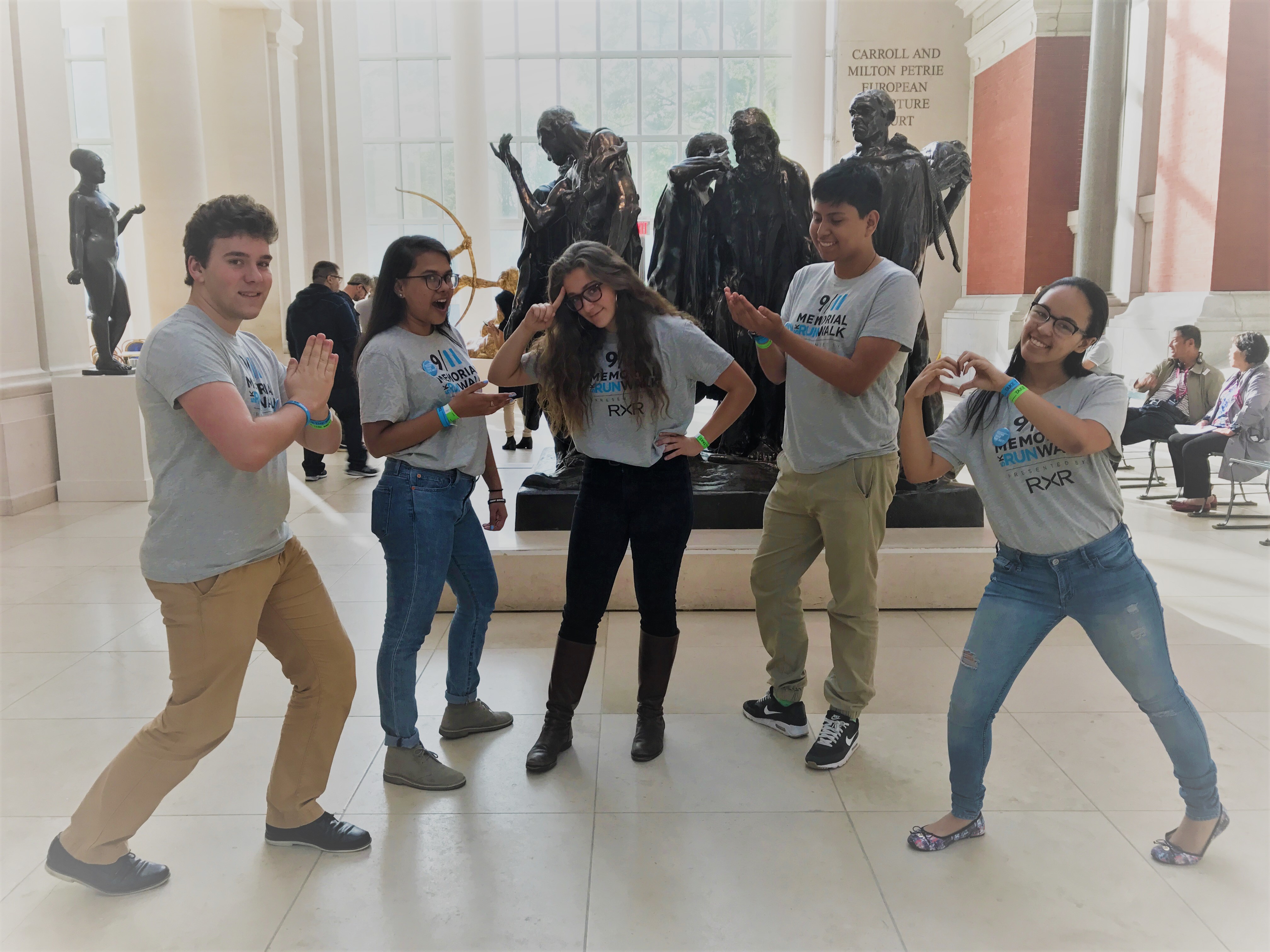A group of 9/11 Museum ambassadors—two young men and three young women—strike a pose in the European sculpture gallery at the Metropolitan Museum of Art. Several sculptures stand behind them.
