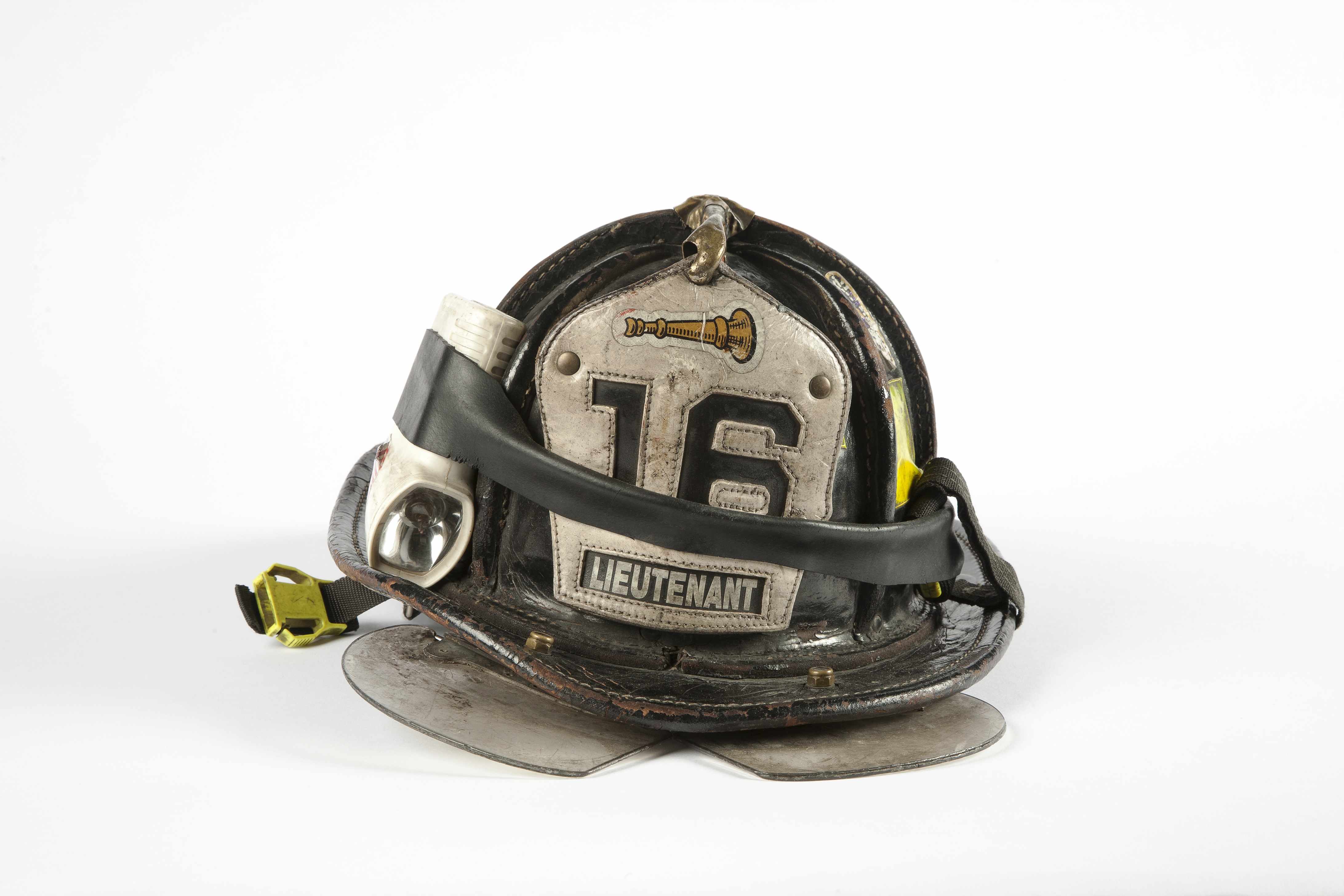 A black and white firefighter helmet with the number 16 and the word lieutenant on it is displayed on a white surface at the Museum.