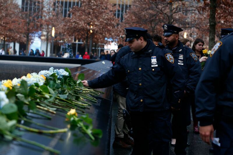 NYPD officers lay yellow and white flowers on a bronze parapet inscribed with the names of victims at the 9/11 Memorial.