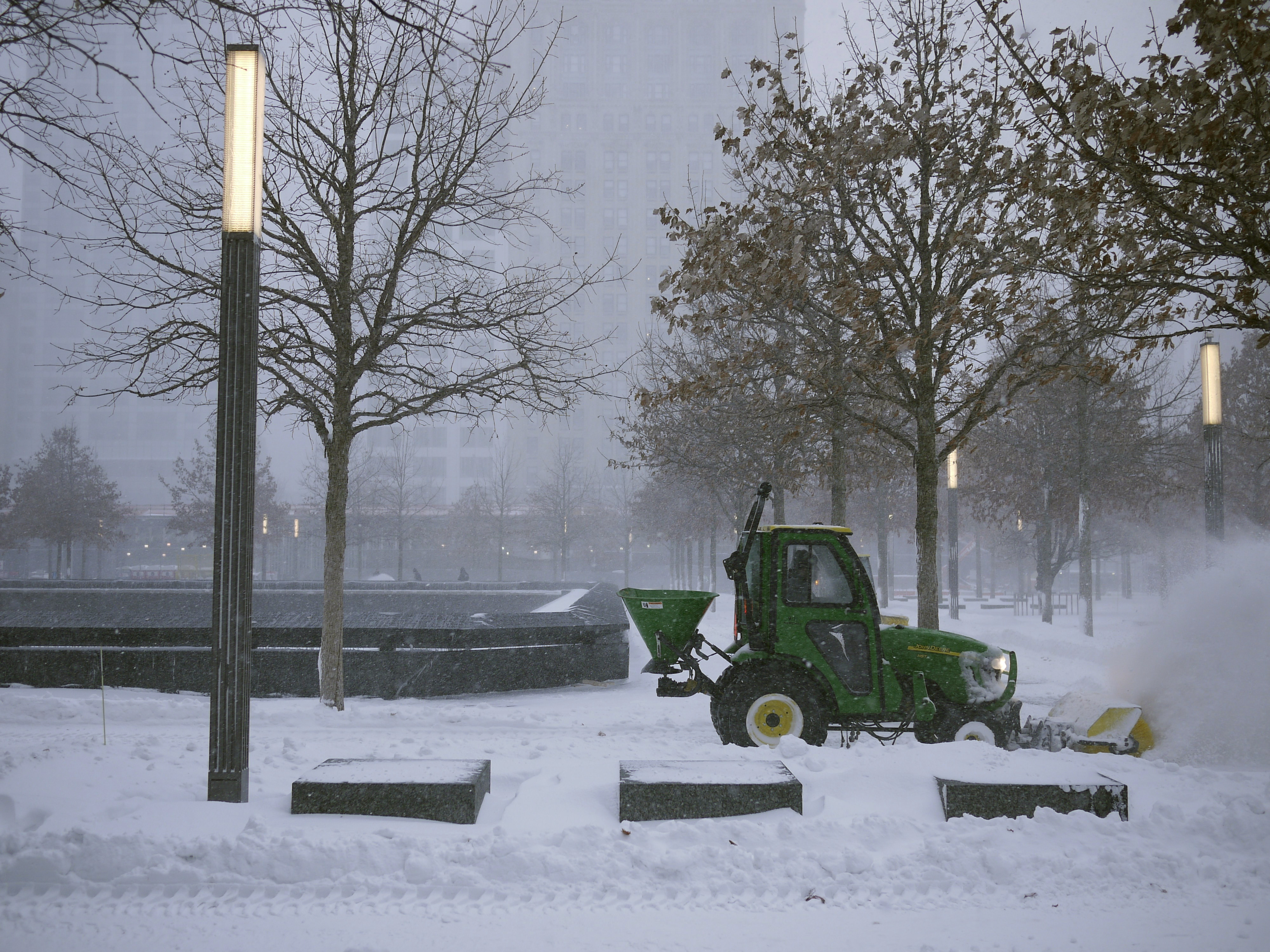 A man driving a green plow clears snow from the 9/11 Memorial during a snowstorm.