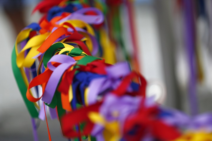 An abundance of rainbow-covered ribbons are loosely tied around a barrier in an act of memorialization.