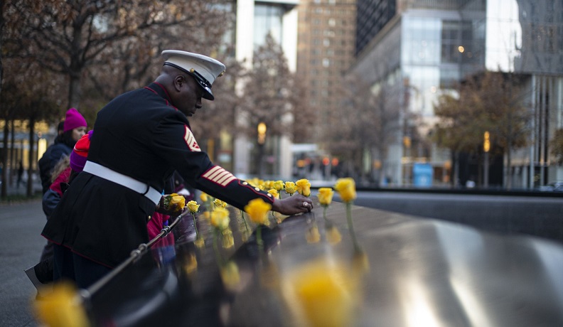 A Medal of Honor recipient in dress uniform places yellow roses on the 9/11 Memorial parapets.