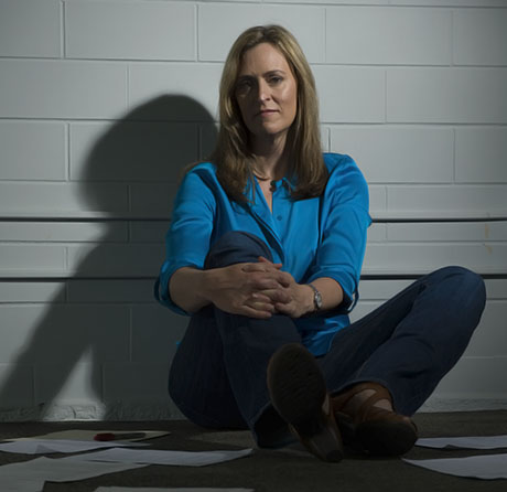 A woman sits with crossed legs in front of a white wall.