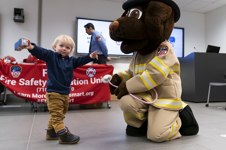 A blond toddler stretches his arms to greet a man in a dog suit.