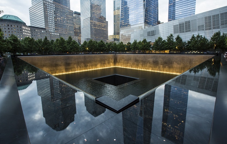 The glare of an overcast, late-afternoon sky reflects off the water within the Memorial Pool.