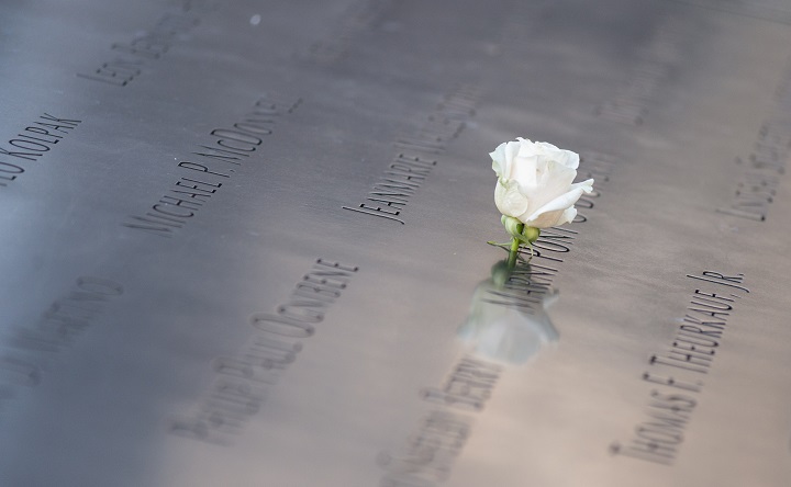A single, white rose is placed at a name etched on a bronze parapet of the Memorial.