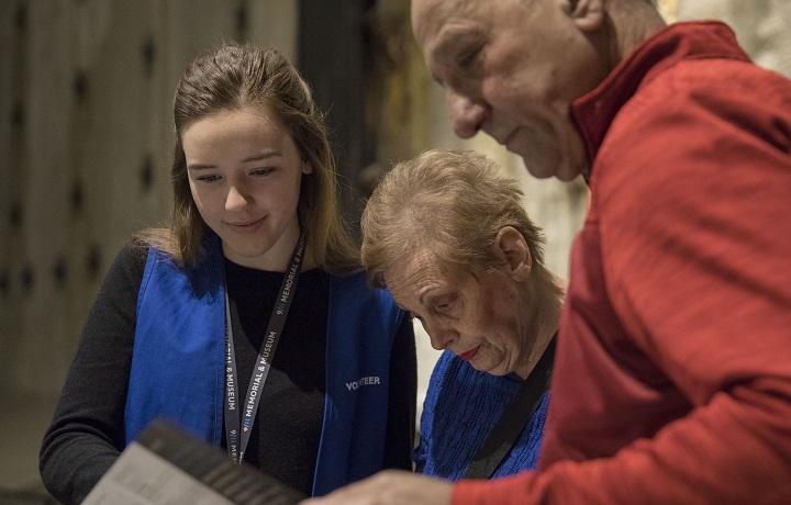 A volunteer wearing a distinctive blue vest shows visitors where they are within the 9/11 Memorial museum by using a handheld paper map.