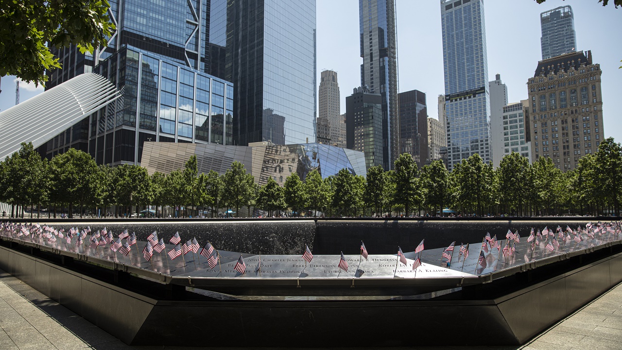 A view of American flags inserted into the names parapet. In the background are the skyscrapers of the World Trade Center.