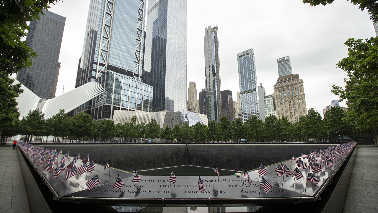 A view of American flags inserted into the names parapet. In the background are the skyscrapers of the World Trade Center.