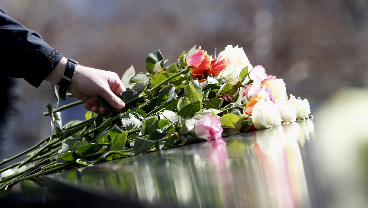 A hand places a long-stemmed rose on the memorial parapet.