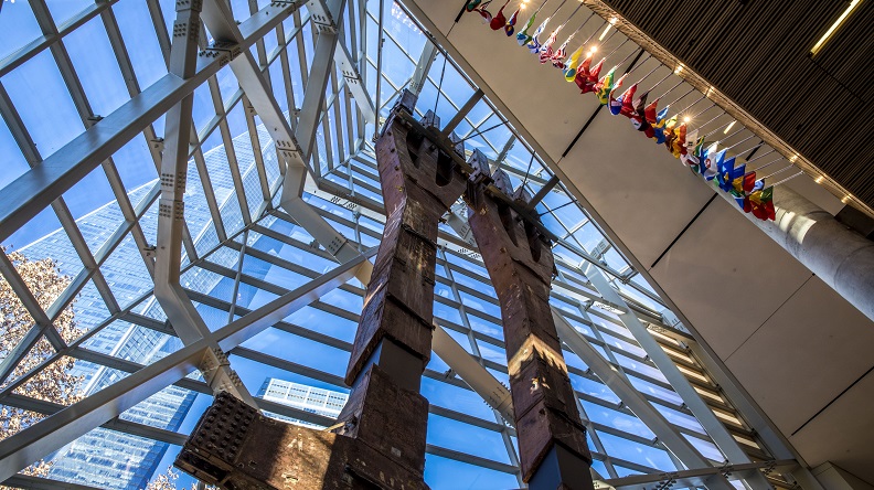 Two eighty-foot tall steel columns, known as the Tridents, tower over the interior of the museum Pavilion. One World Trade Center points skyward outside the windows.