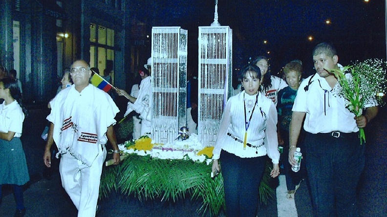 A man and a woman hold aloft a silver folk-art sculpture of the Twin Towers resting on a bed of artificial grass.