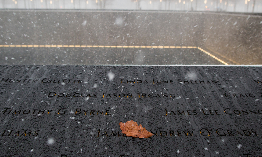 Snow falls on the 9/11 Memorial while a yellow leaf rests on the bronze parapets. 