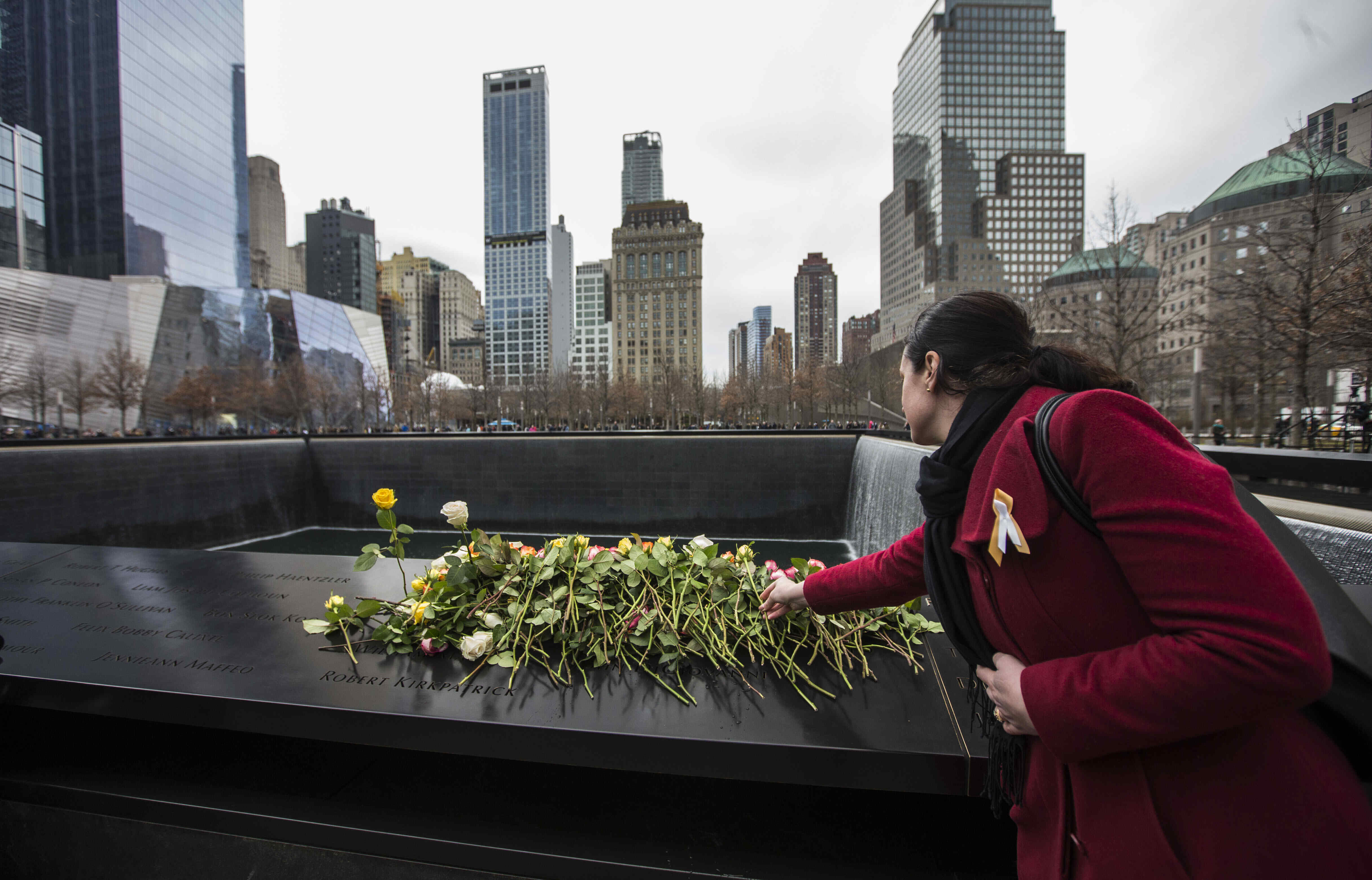 A woman in a red winter coat place a rose atop other flowers left on panel N-73 of the 9/11 Memorial's North Pool to commemorate the victims of the 1991 attack on the World Trade Center. 