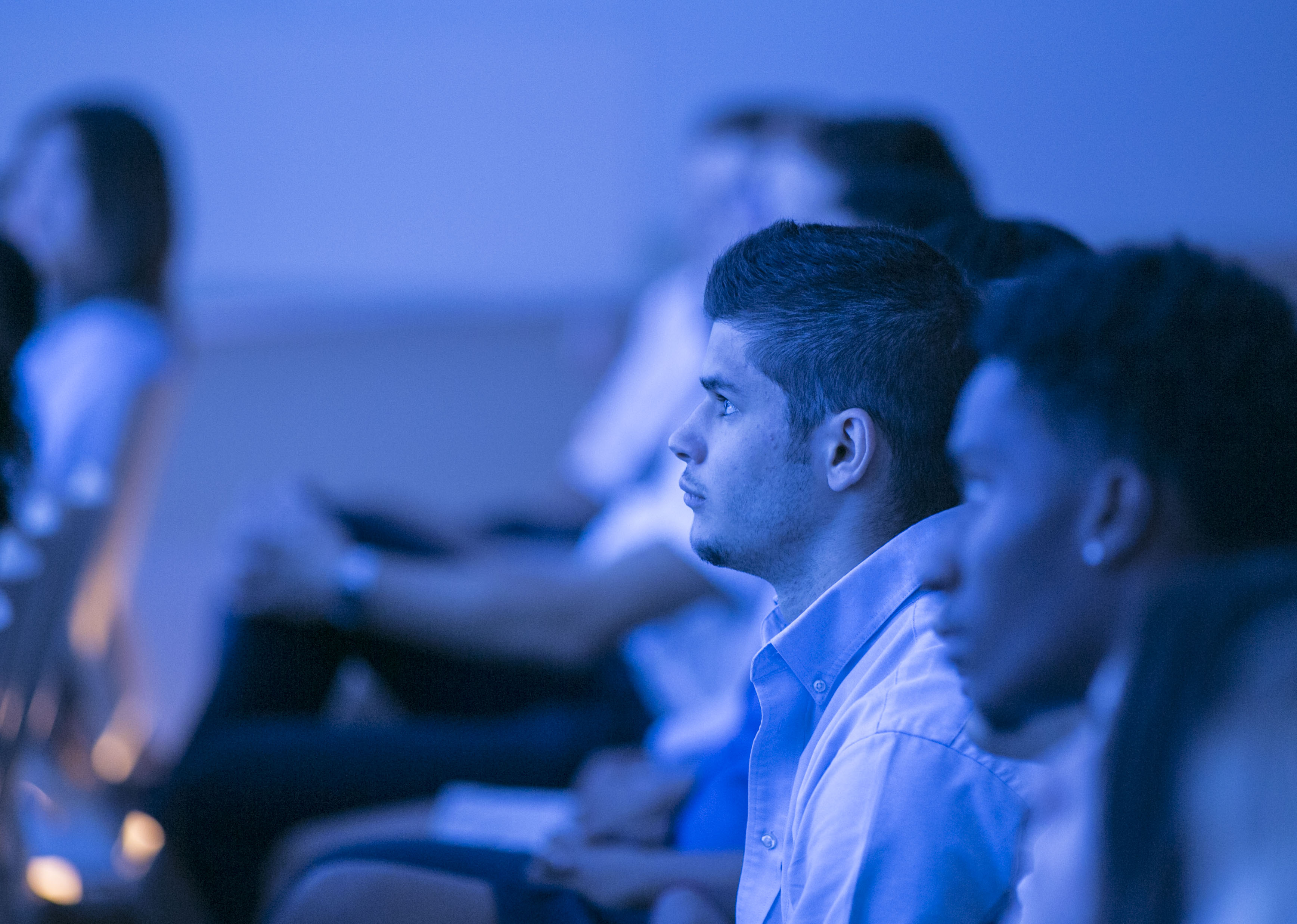 A row of students, cast in a blue light from a presentation, pay close attention during the Anniversary in Schools Webinar.