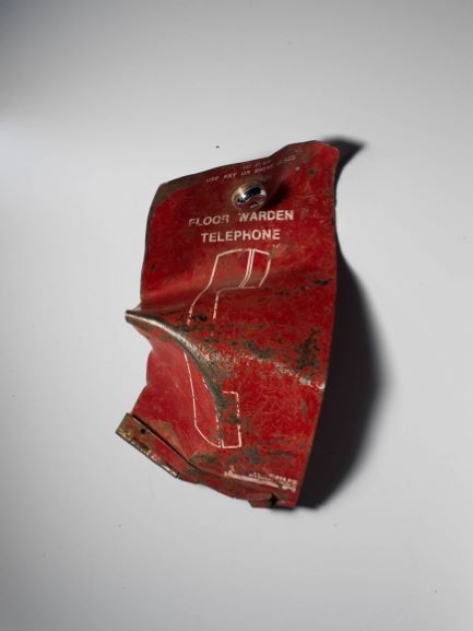 Warped red metal fragment of lock box panel from floor warden emergency telephone