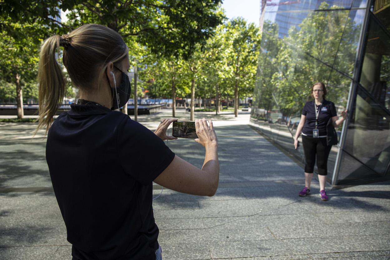 Back view of a blonde woman with a ponytail in a navy blue shirt recording a co-worker, dressed in a navy blue top with black leggings, as she speaks outside of the Museum.