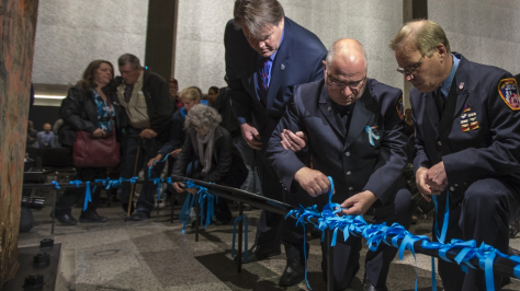 Three men tie blue ribbons around the metal base of an exhibit