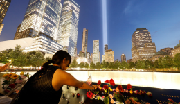 Back view of a woman placing flowers on the Memorial at night, with the Tribute in Light visible in the darkened sky