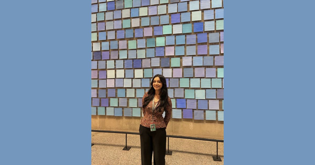 A woman stands in front of a wall of tiles in different shades of blue. 