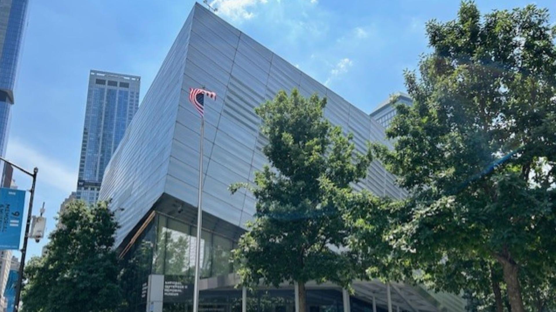 Exterior of the Museum, against a blue sky and green trees. An American flag sways in the breeze.