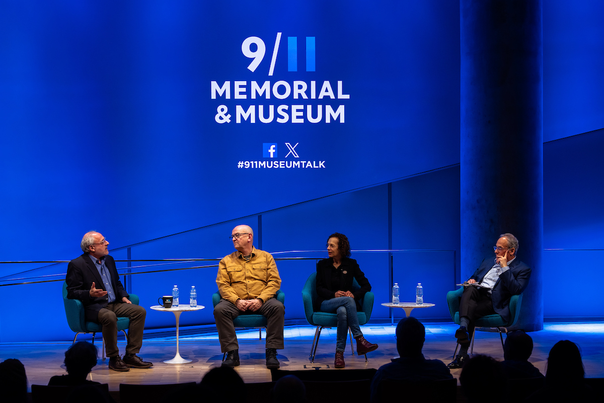 Four panelists seated on a stage with a giant screen behind them showing the opening 9/11 Memorial and Museum's logo and social icons