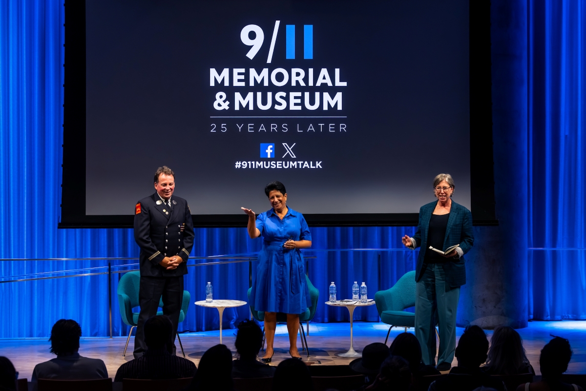 Three people stand on stage in front of a 9/11 Memorial & Museum logo