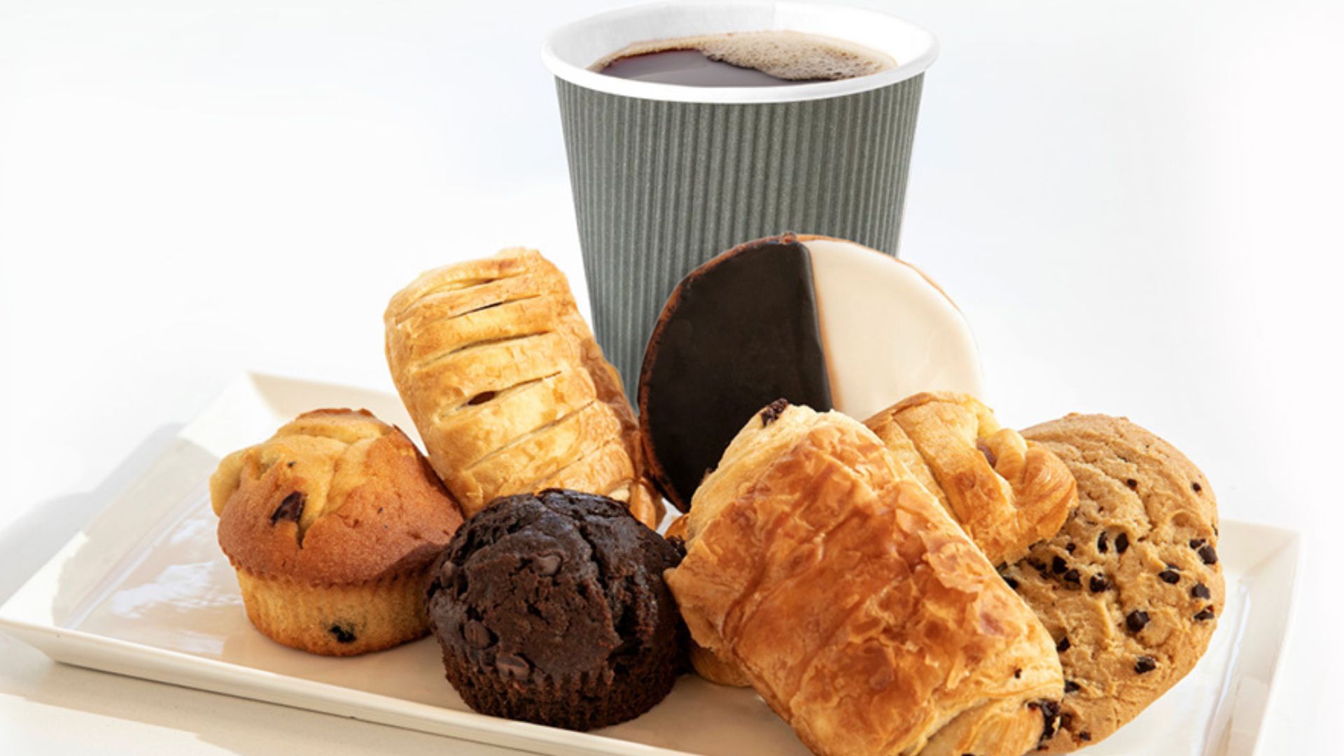 A cup of coffee on a tray, surrounded by pastries