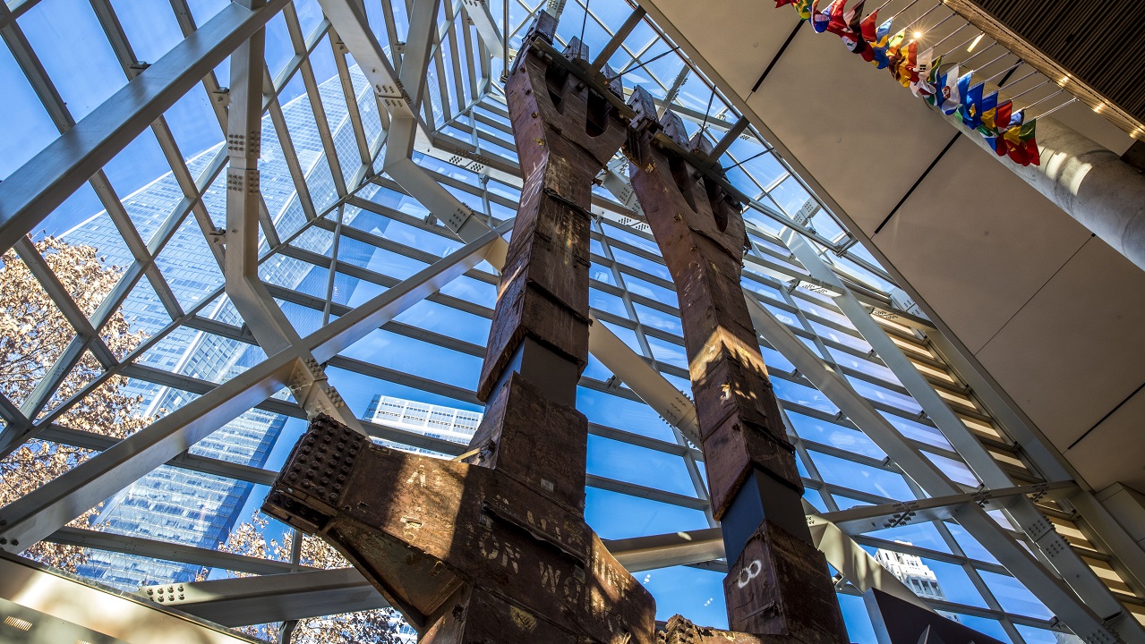 Two eighty-foot tall steel columns, known as the Tridents, tower over the interior of the museum Pavilion. One World Trade Center points skyward outside the windows.