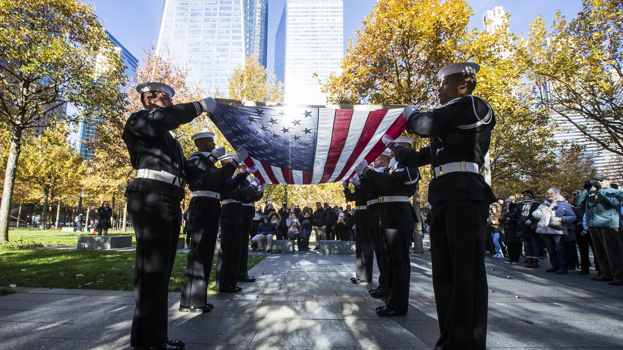 Members of the U.S. Navy hold a flag-folding ceremony on the 9/11 Memorial plaza before a group of onlookers.