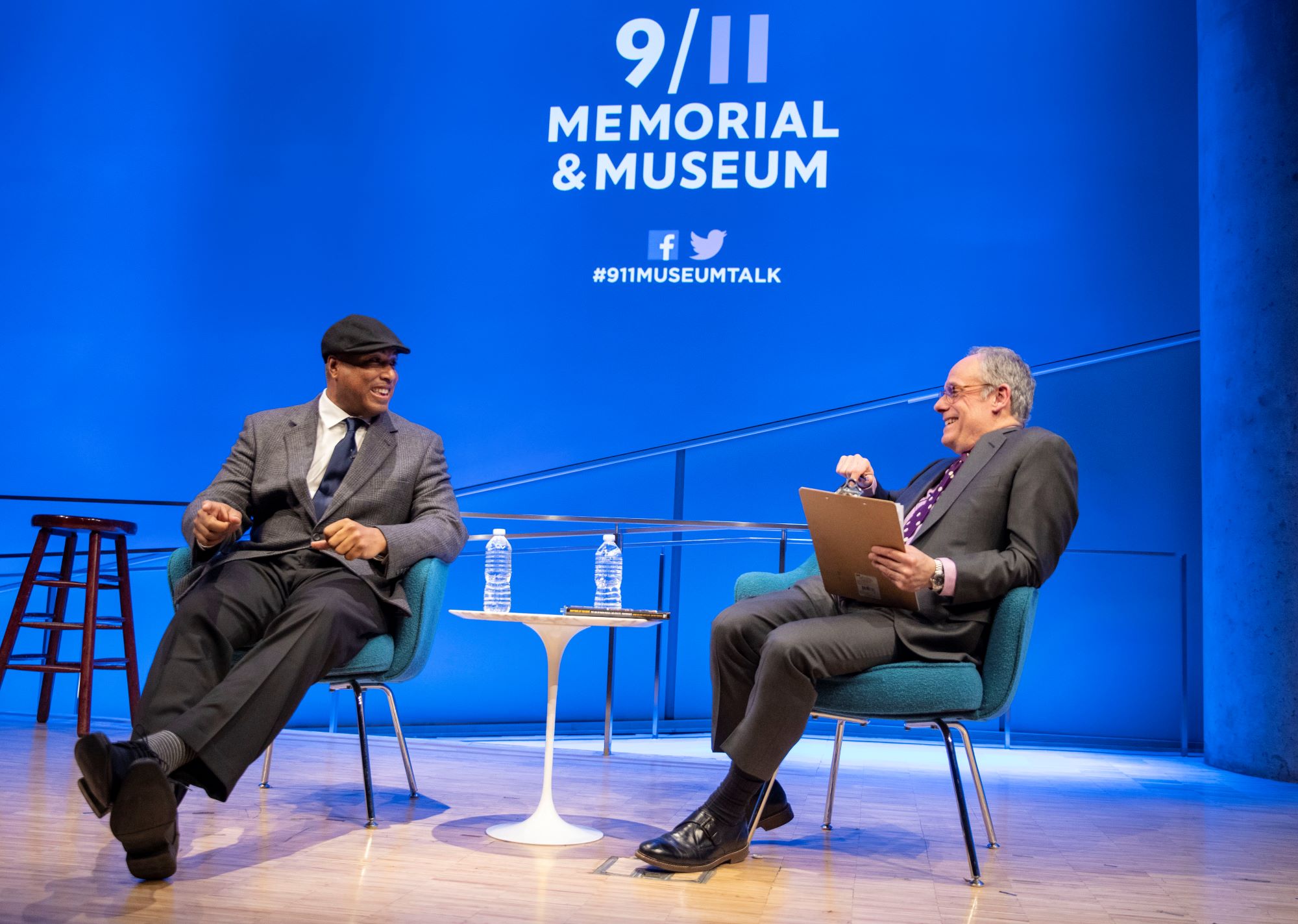 Former Yankees player Bernie Williams is interviewed by Clifford Chanin, the executive vice president and deputy director for museum programs, onstage at the Museum Auditorium. Williams is sitting with his feet out and crossed while Chanin is smiling and holding a clipboard.